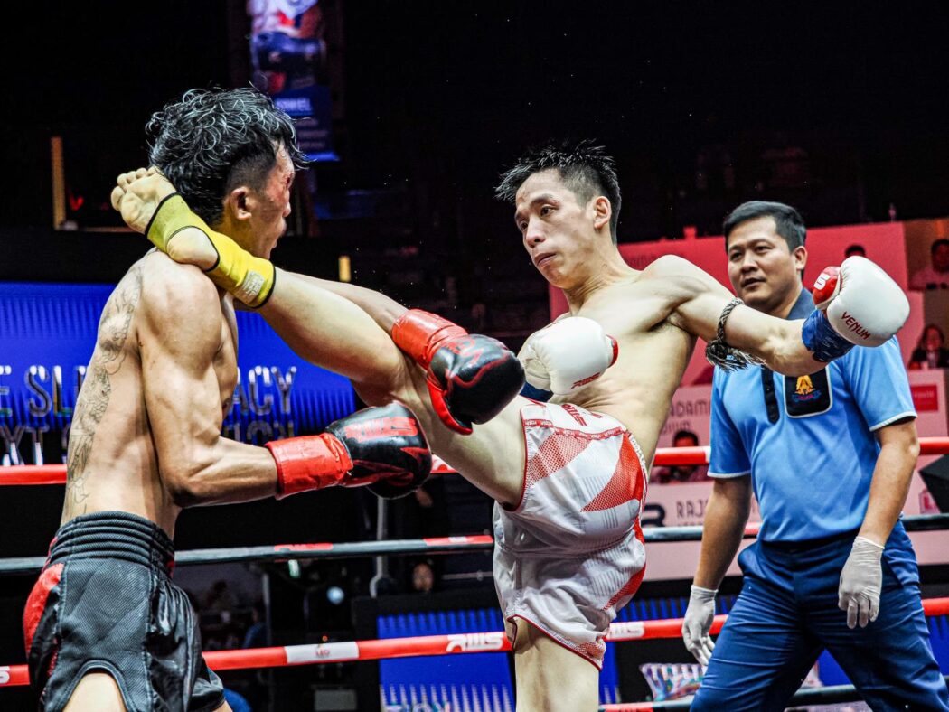 a Muay Thai fighter in white trunks lands a high kick to his opponent’s neck