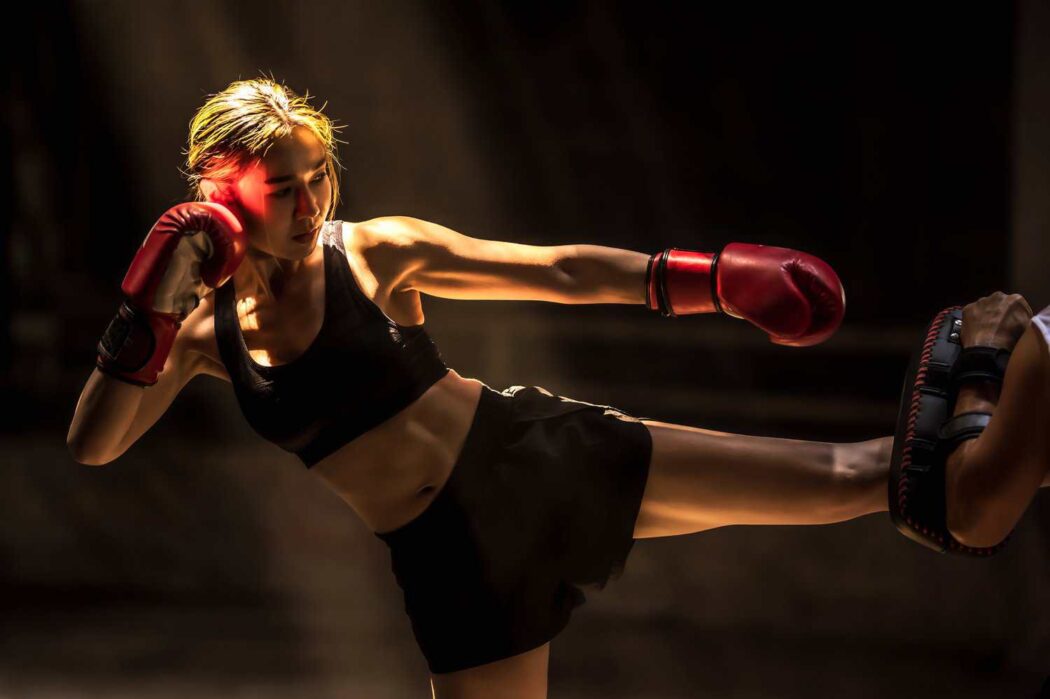 woman trains muay thai with a coach holding a kick shield
