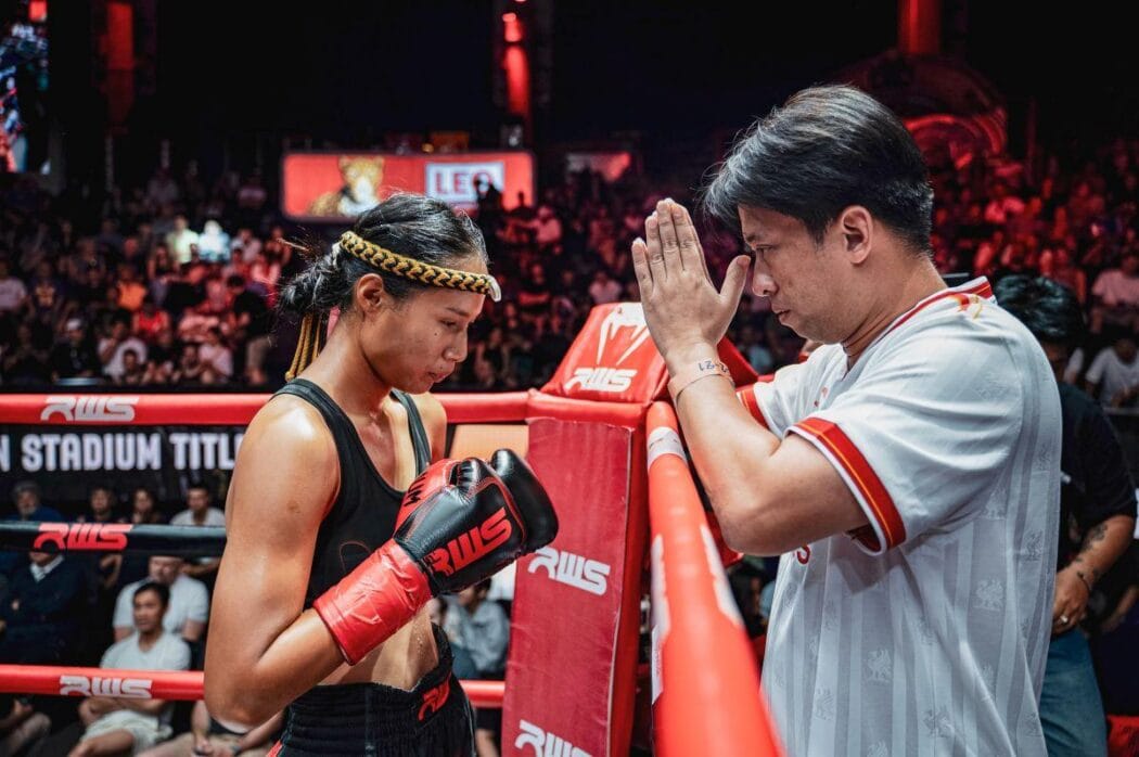 A Muay Thai trainer encourages a practitioner in the ring.